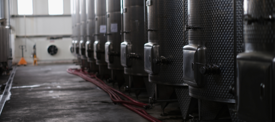 . The tanks are equipped with valves and piping. There are red hoses on the ground, and the environment looks industrial with a concrete floor. It appears to be an interior setting with artificial lighting.