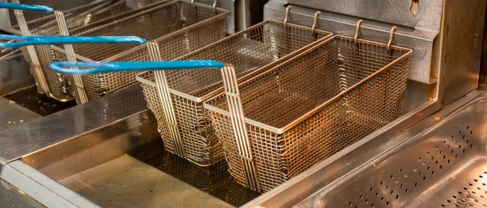 The image shows the interior of a commercial deep fryer with empty metal baskets, indicating it's not currently in use.