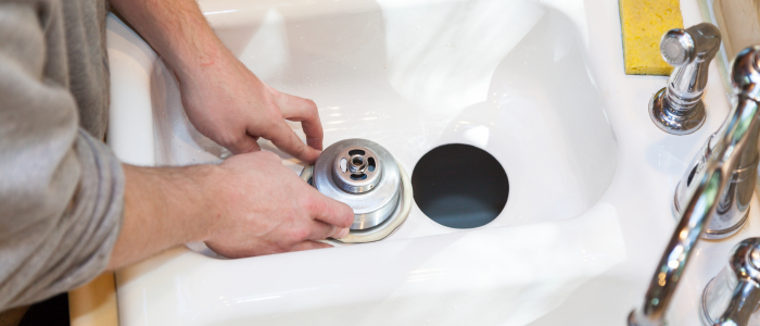 The image shows a person's hands installing or repairing a garbage disposal unit in a white kitchen sink.